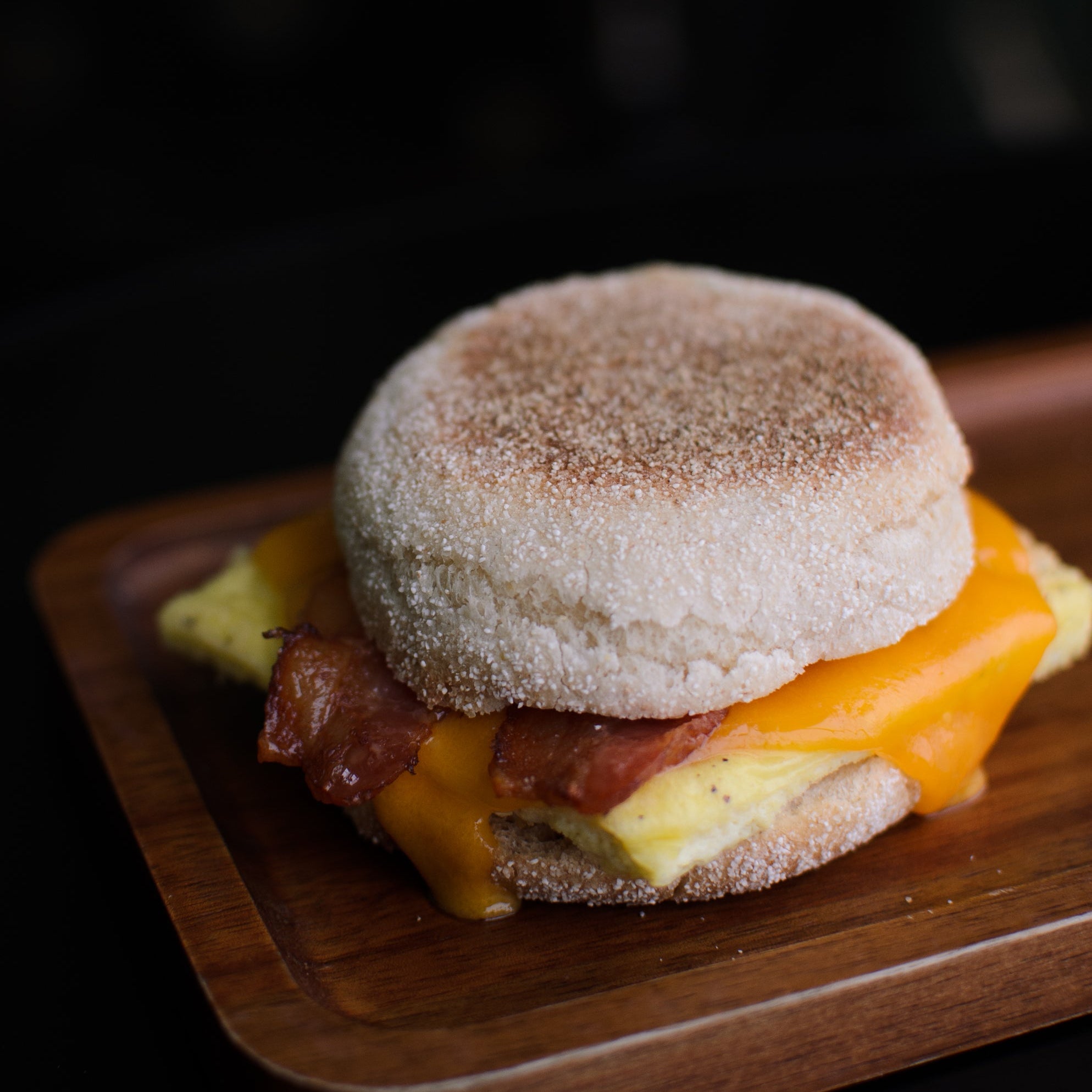 Breakfast sandwich with bacon and cheese on a wooden board against a dark background